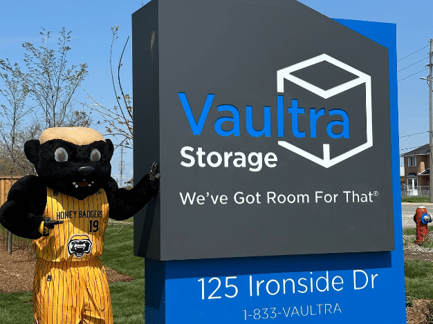 Grand opening event at Vaultra Storage Brampton with a friendly honey badger mascot interacting with guests, festive decorations, balloons, and a ribbon-cutting area, creating a welcoming and lively atmosphere.